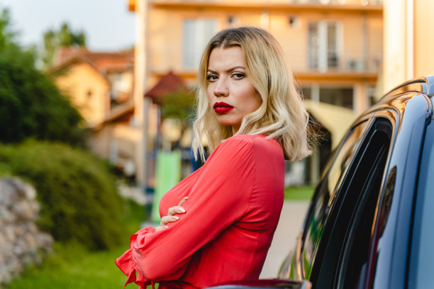 在夏日的户外，一名疯狂的白人成年女性穿着衣服，双手交叉，倚靠在汽车上，愤怒地看着镜头的侧面照片图片下载