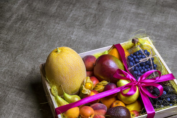各种成熟的水果和浆果被漂亮地堆放在木制的盒子里，用粉红色的丝带扎好。黑暗的背景。送餐，礼品水果套装。健康饮食的概念。副本的空间。有选择性的重点。图片下载