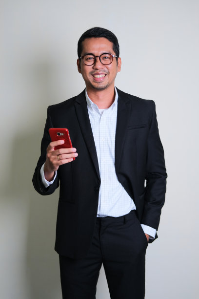 穿着黑色西装的亚洲商人手拿智能手机，面带自信的微笑图片下载