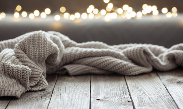 舒适的背景与针织元素在木制表面和散景灯。图片下载