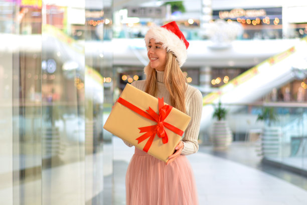 购物中心的快乐女孩，戴着圣诞帽，拿着礼盒。假日购物和礼物。销售。购物中心图片下载