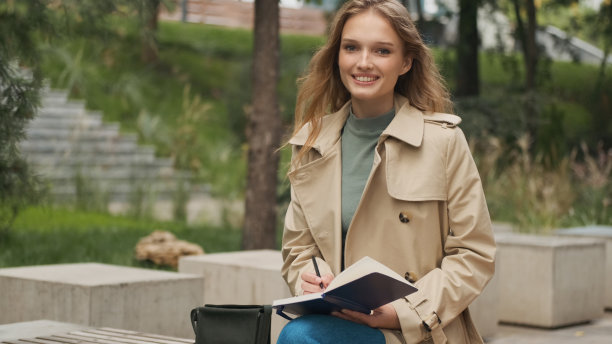 美丽的积极的学生女孩微笑着在城市公园的长椅上做大学作业。时尚女孩在户外学习。研究概念图片下载