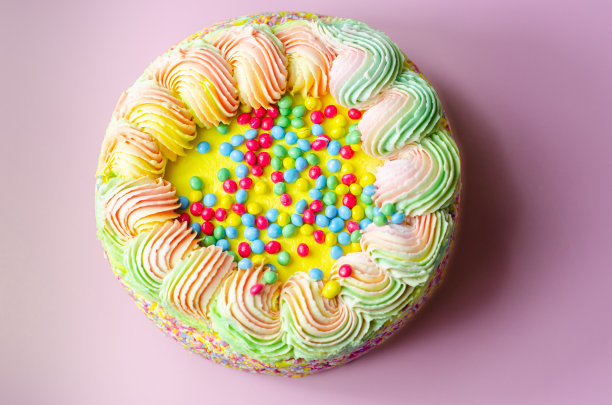 马德拉海绵蛋糕上涂有黄色糖霜，层有李子和覆盆子果酱，里面和上面有五颜六色的巧克力粒，装饰有五颜六色的糖霜和糖装饰图片下载