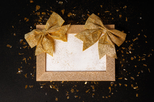 金色框架从闪光与一个黑色背景上的金色蝴蝶结。贺卡。副本的空间。新年贺卡背景。特写。简单的简约。图片下载