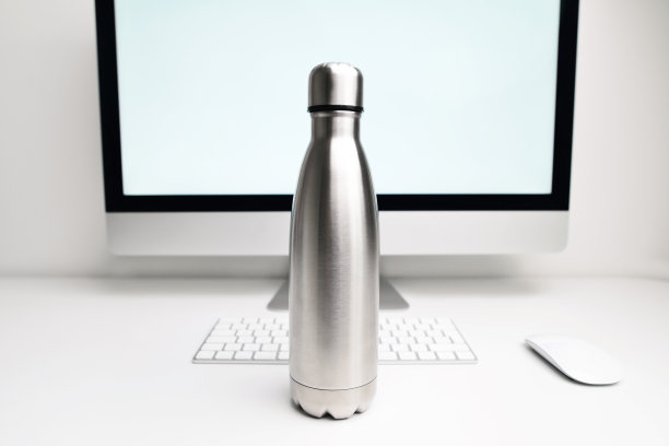 办公室桌子上电脑和文件旁边放着装水的钢制热水瓶。黑色哑光，空不锈钢热水壶特写。不锈钢热水瓶。图片下载