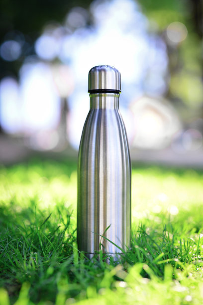 绿色草地上可重复使用的钢制热水瓶。银钢热水瓶，背景上模糊的草与复制空间。是塑料的自由。“零浪费”。副本的空间。垂直的照片。图片下载