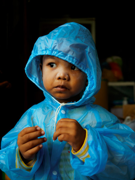 皮肤黝黑的亚洲男孩穿着蓝色雨衣，以防止身体在雨天被淋湿图片下载