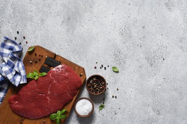 生牛肉和香料盐放在木板上。鲜肉在混凝土的背景上，一张餐巾纸和一个地方的文本。图片下载