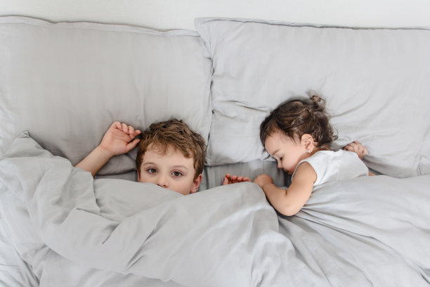 弟弟醒了，看着镜头，但他的妹妹还在睡觉图片下载