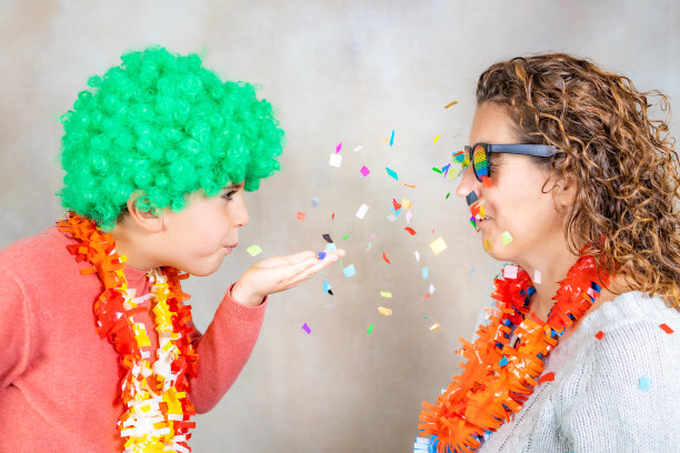 在狂欢节上向妈妈吹五彩纸屑的滑稽小孩图片下载