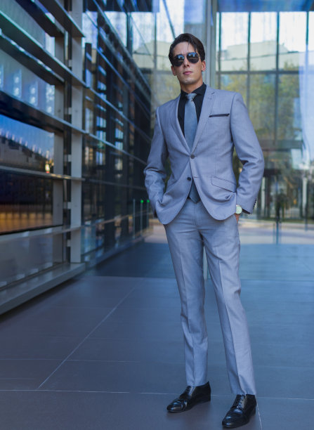 一位优雅的男士，穿着正式的职业装，双手插在口袋里，站在办公楼的入口处图片下载