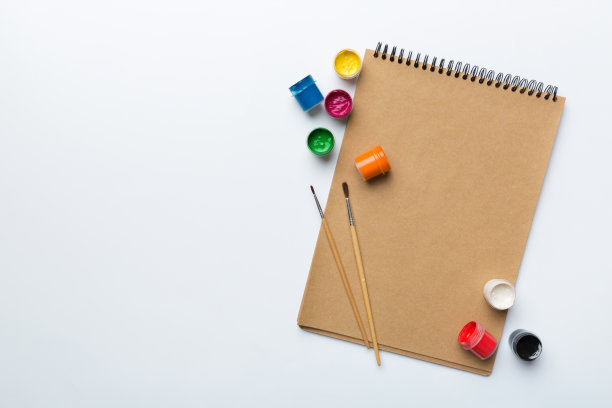 相册页和油漆，铅笔，画笔上的彩色背景。顶部视图与空的空间。工作场所的创造力。家庭教学概念图图片下载