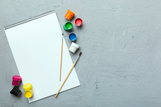 相册页和油漆，铅笔，画笔上的彩色背景。顶部视图与空的空间。工作场所的创造力。家庭教学概念图图片下载