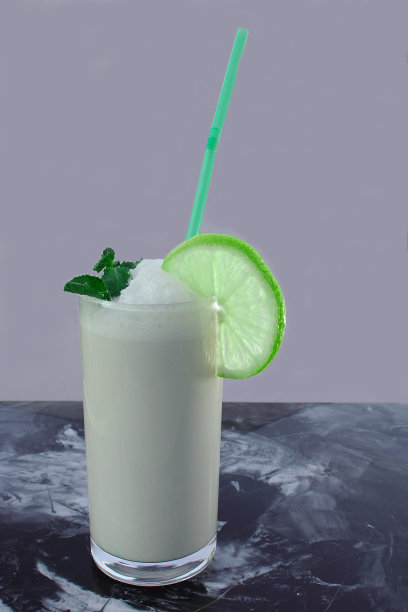 桌上放着高脚杯里的牛奶酸奶鸡尾酒，上面点缀着一片柠檬和薄荷。图片下载