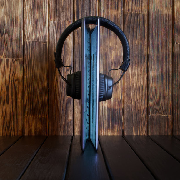 一个发光的笔记本电脑支架，配上耳机，放在木制的背景上。利用现代科技和互联网收听音乐、广播、播客和音频博客的概念图片下载