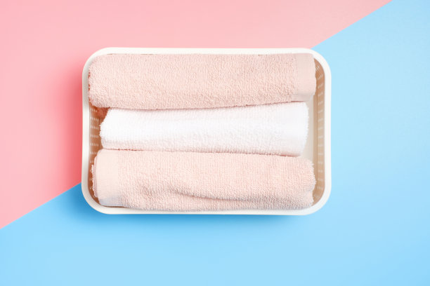 折叠的毛巾躺在粉色和蓝色背景的塑料容器里，近距离俯视图。图片下载