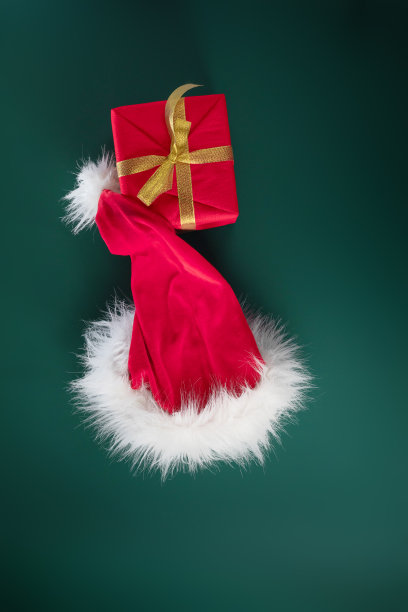 平坦的红色圣诞老人的帽子与毛茸茸的皮毛和礼物盒在绿色的背景。节日的概念，圣诞新年派对，特价。图片下载