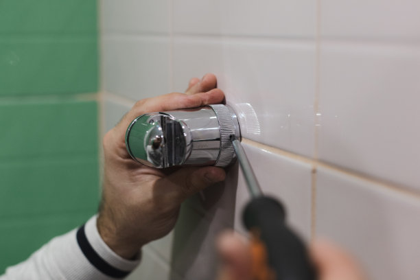 特写镜头，男人的手安装和安装淋浴喷头支架与十字螺丝刀的帮助，瓷砖墙在洗手间。浴室装修工程。翻新工程产生的污垢图片下载