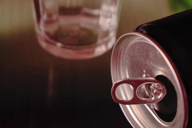 黑色的铝罐，躺在一个棕色的表面上，底部是一个模糊的玻璃烧杯的一部分。图片下载