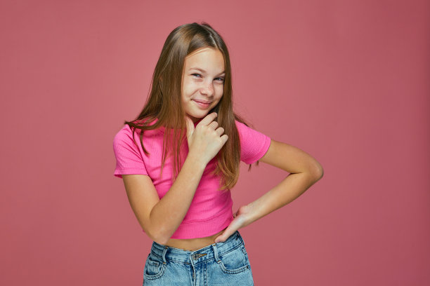 调皮捣蛋的小女孩摸着下巴策划恶作剧，看着粉色画室背景的摄像机图片下载