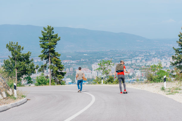 身材高大的运动员穿着红色t恤和黑色牛仔裤，快速平稳地骑着长板下坡。图片下载