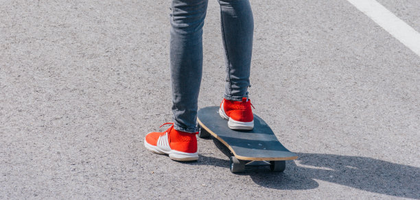 男性白人滑板运动员在一条空路上滑下坡，做一个快速折弯和抓板，同时快速驾驶长板。红t恤，绿帽子，黑牛仔裤。图片下载