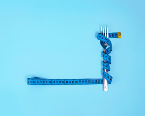 金属叉子和蓝色卷尺在蓝色的背景上测量图片下载