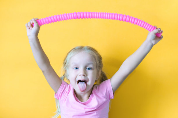 流行管。抗压力感觉塑料玩具从一个流行管在一个孩子的手中。快乐的小女孩玩着一个玩具，烦躁的流行音乐管。2021年的趋势。图片下载