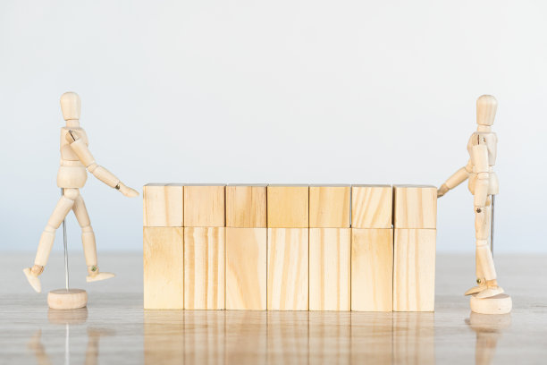 2木木偶构建一个木制桌子上墙,白色背景,保护概念。图片下载