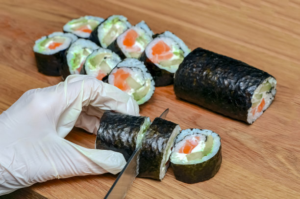 制作日本寿司的过程。手拿刀在木板上切一个卷图片下载
