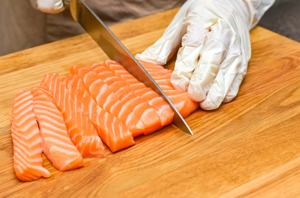 厨师的手合上了。在一块木制的切菜板上，厨师用刀切一条红色的鱼图片下载