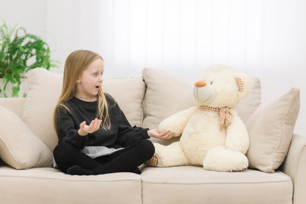 小女孩和她的白色泰迪熊在沙发上聊天的照片。图片下载