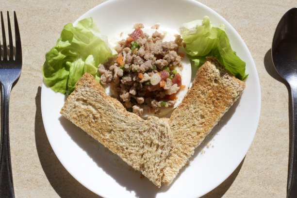 早餐照片，简单的早餐，排列在心形，在花园里，包括面包，蔬菜，煮猪肉碎在白色的盘子，棕色的瓷砖作为背景。图片下载