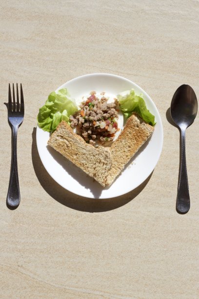 早餐照片，简单的早餐，排列在心形，在花园里，包括面包，蔬菜，煮猪肉碎在白色的盘子，棕色的瓷砖作为背景。图片下载