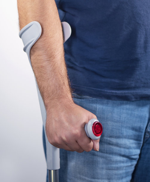 一个拄着灰色拐杖的残疾男性。只有他的胳膊和身体。身体损伤，断腿。交通事故，工作事故。图片下载