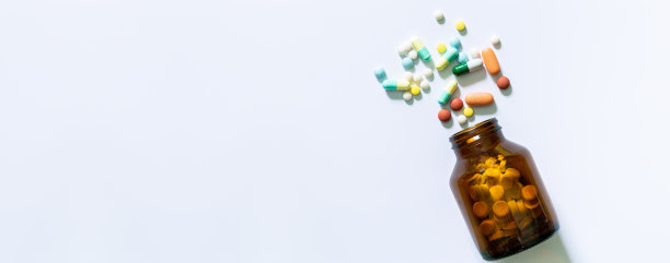药丸和药丸瓶在白色背景，彩色药丸和棕色瓶子在蓝色背景与复制空间。前视图。保健、医药和药学概念图片下载