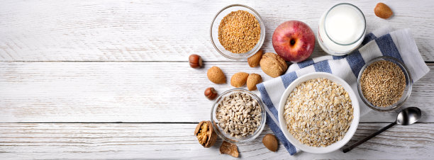 早餐有燕麦，亚麻籽，葵花籽，芝麻，牛奶，苹果，核桃，杏仁和榛子，白色木材背景。俯视图，文本空间。图片下载