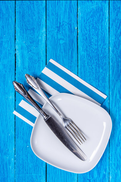 背景与空方白色陶瓷板和银餐具蓝色木板。Copyspace。垂直的照片。图片下载
