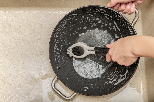 一个女人在洗煎锅，一只手在厨房水槽里洗煎锅，一个女人在用硅胶刷洗盘子。文本的地方图片下载