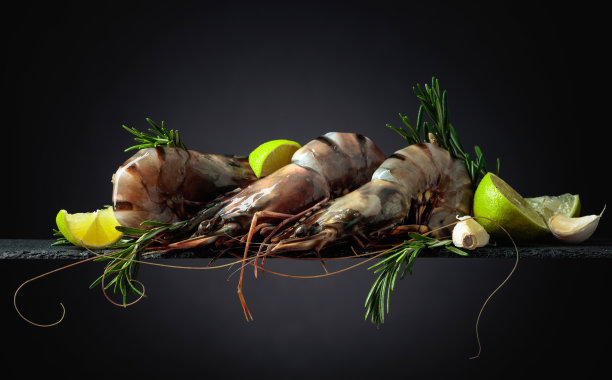 新鲜的虎虾配上青柠，迷迭香和大蒜，以黑色为背景。图片下载