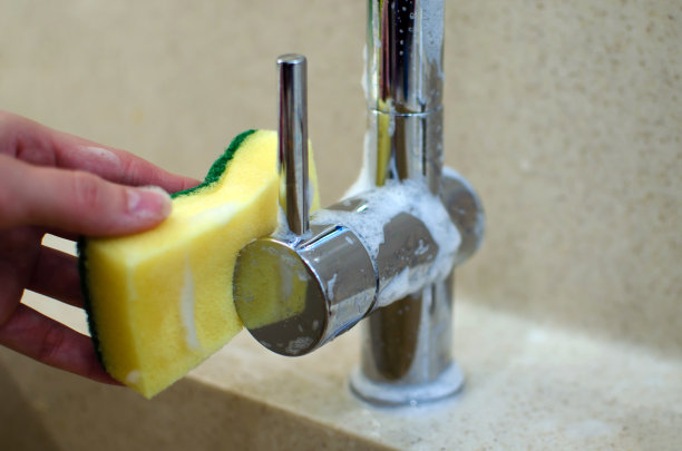 女性手洗镀铬水龙头与黄色海绵在新的现代厨房，台面坚实的表面图片下载