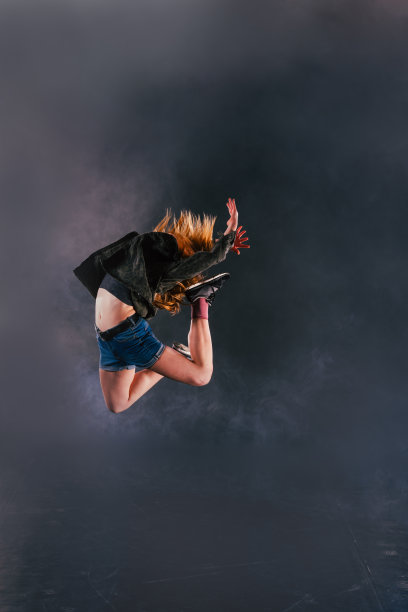 弹力女舞者在烟雾缭绕的背景下跳得很高。图片下载