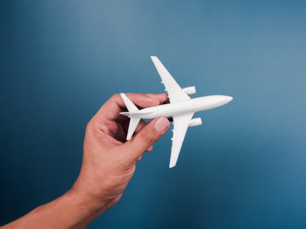 手握白色飞机玩具模型上的蓝色背景，俯视图，最小的风格。白色飞机，平铺设计。飞行中,旅行的概念。图片下载