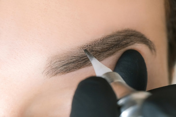 美容师使永久眉妆在一个美丽的年轻女子的脸上。图片下载