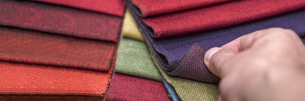 不同颜色和厚度的室内装潢用纺织品样品。多色织物纹理样品的特写细节。一个男人拿了一件布料样品，用手摸来检查它的质量图片下载