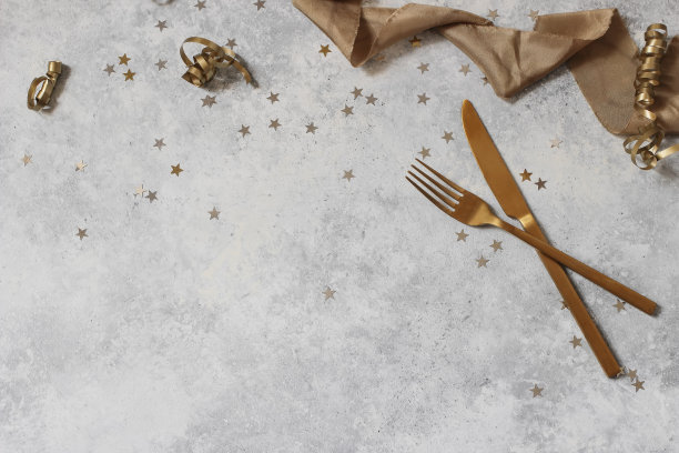 新年静物用金色的彩纸星星、餐刀、餐叉和丝带组成。派对装修，庆典理念。平躺，俯视图。空副本空间。蹩脚货表的背景。图片下载