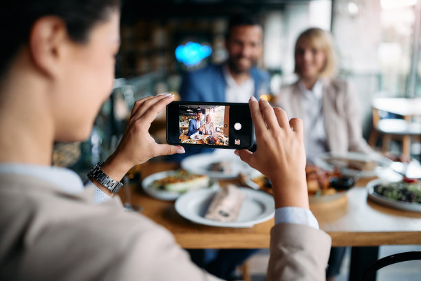 女商人在餐厅午餐期间拍摄她的同事的特写照片。图片下载