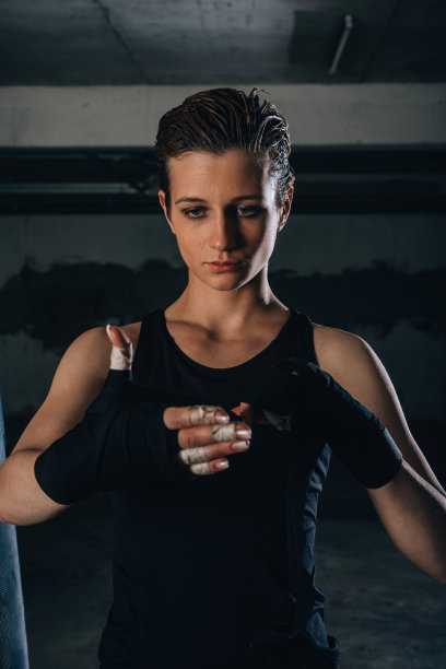 一个年轻强壮的女人的肖像，手腕上缠着黑色绷带，准备在车库里拳击。图片下载