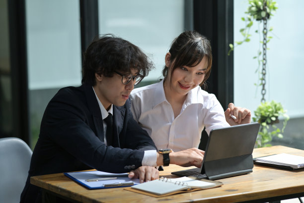 年轻的商务人士使用数码平板电脑，一起坐在木制办公桌前的照片。图片下载