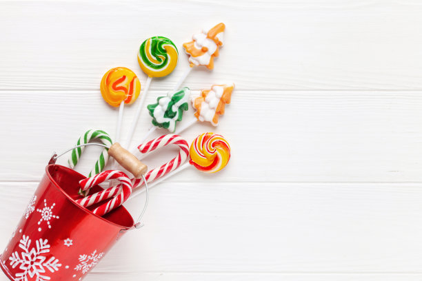 圣诞红桶与节日糖果棒棒糖在白色木制背景。俯视图图片下载